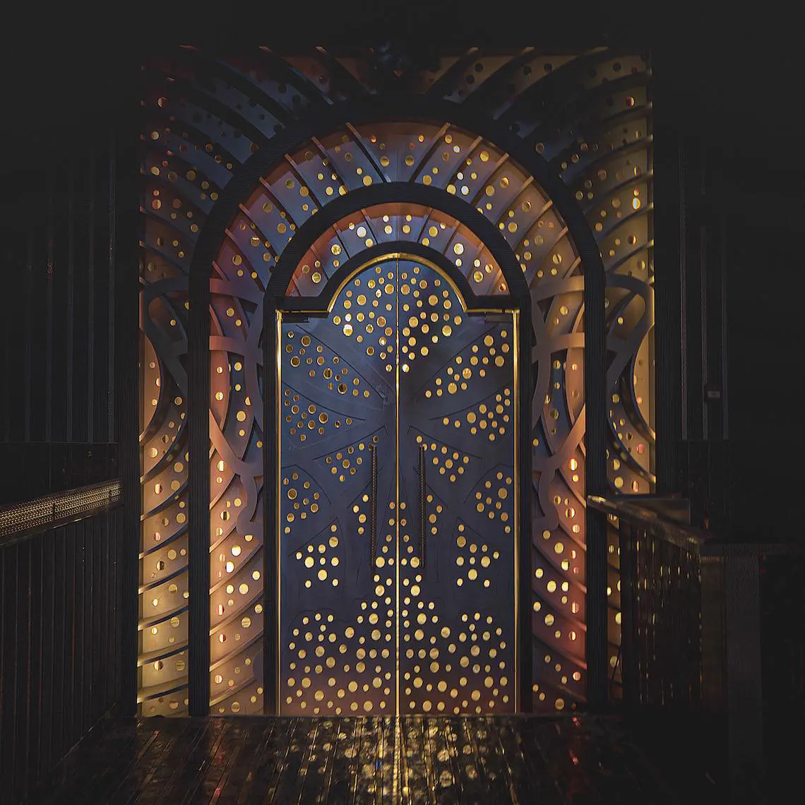 Illuminated arched doorway with concentric fan panels backlit in gold through perforated openings
