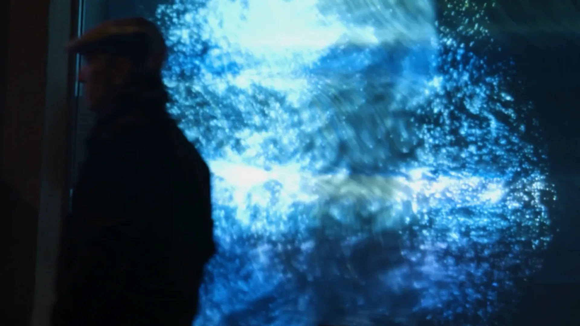 A passer-by silhouetted against blue waves of light on the Ondulations glass façade in Luxembourg