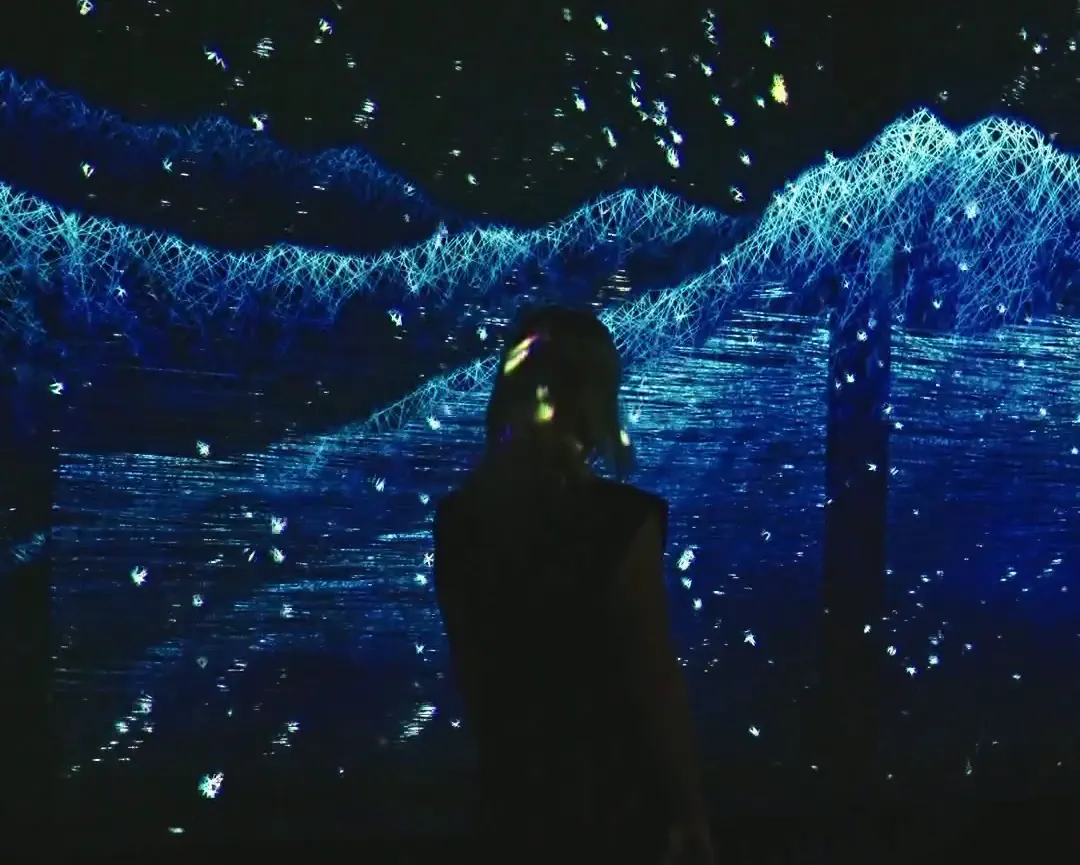 Visitor watching an immersive real-time generative projection of glowing blue point-cloud mountains and drifting light particles